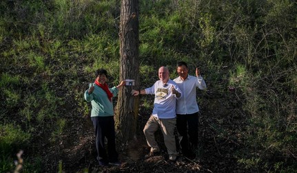 Un copac plantat în urmă cu 26 de ani a crescut în mijlocul fostului teren nisipos. Reîntâlnirea dintre Ronald Sakolsky și Yin Yuzhen este marcată cu o fotografie lângă arborele matur. Sursa foto: Profimedia Images