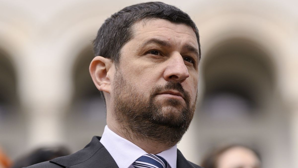 Marius Lulea, vicepreședintele AUR, în prim plan, îmbrăcat cu costum, cămașă albă și cravată albastră