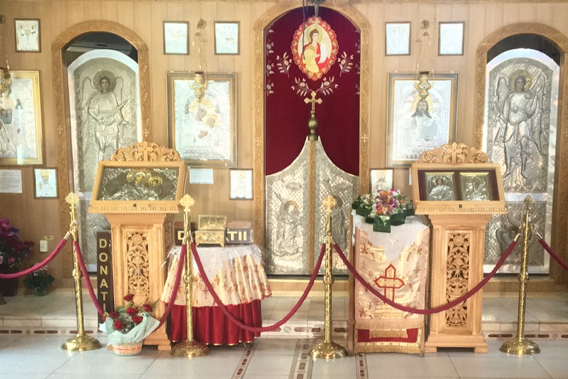 În stânga sunt două dintre cutiile de donații pe care Olaru le golea în altar. Cele două sunt marcate cu „DONAȚII” și așezate în biserica de lemn din curtea parohiei, care cuprinde și o biserică mai mare, de beton.