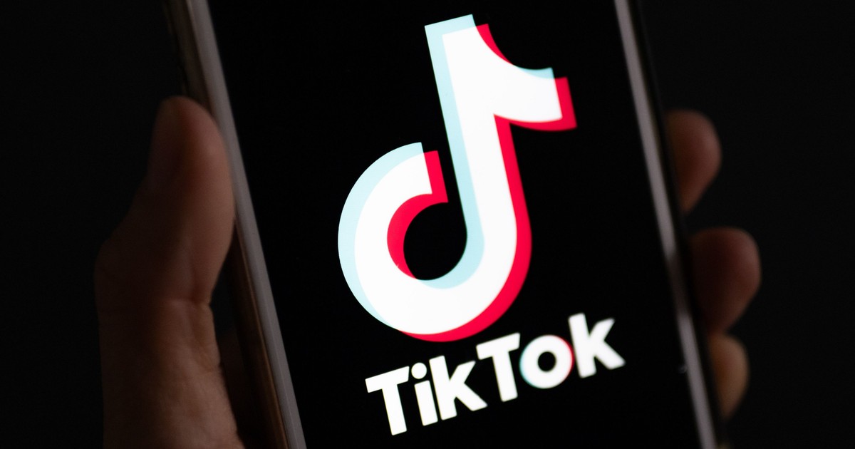 Imagine cu o mână în care se află un telefon mobil pe ecranul căruia este afișat logo-ul TikTok