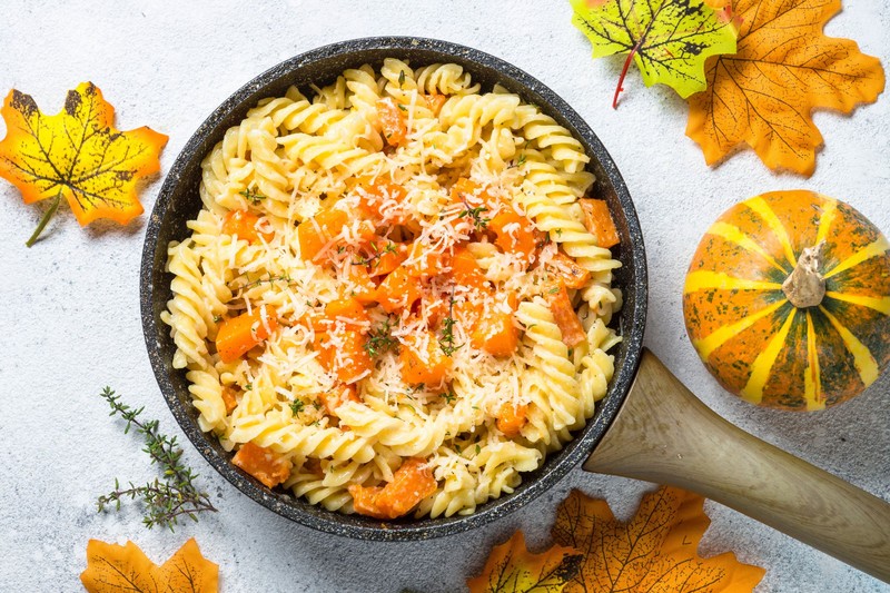 Autumn dish. Pumpkin pasta with cream sauce and parmesan in skillet on stone table. Top view.