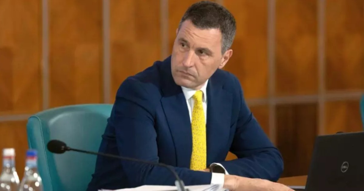 Tanczos Barna așezat la birou în timp ce privește într-o parte și poartă o cravată foarte galbenă
