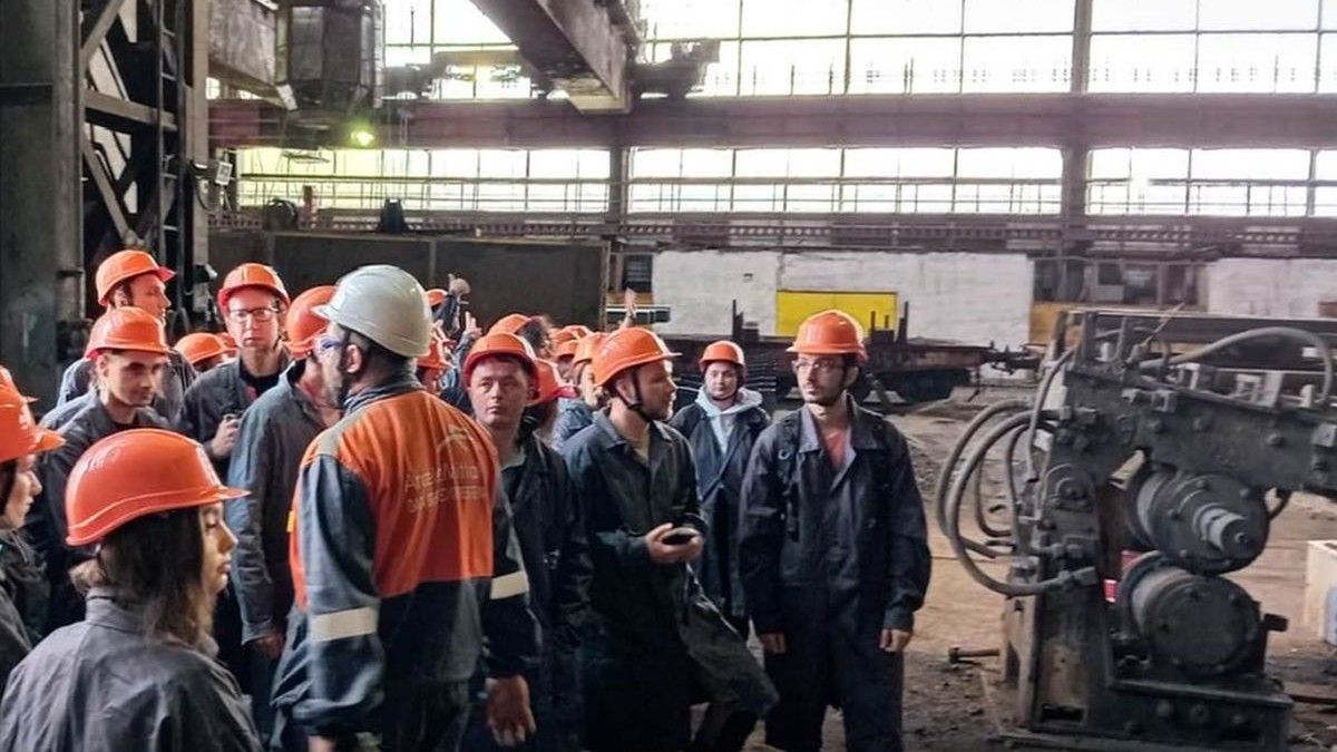 Mai mulți bărbați cu căști portocalii de protecție pe cap sunt într-o hală a combinatului ArcelorMittal Hunedoara