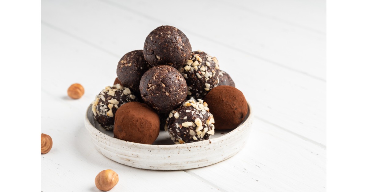 Bomboane rotunde de ciocolate intr-un bol alb pe masa asezate in forma de turn. Unele au cacao pe deasupra sau alune sfaramate