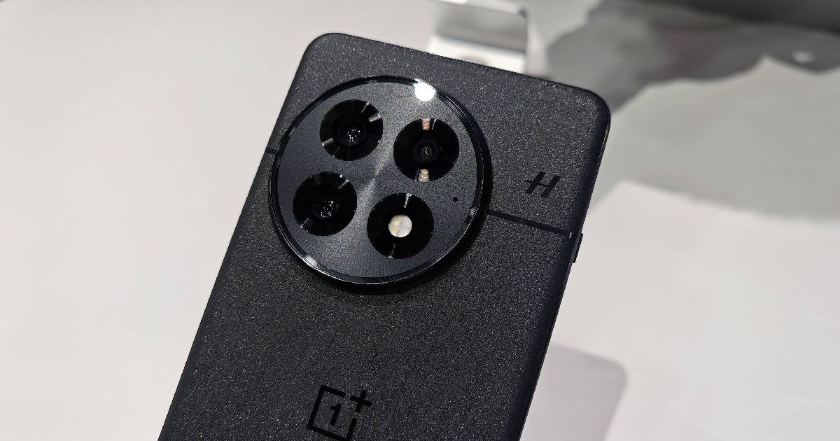 Un telefon OnePlus 13 gri, cu spatele spre privitor, pe un fundal alb.