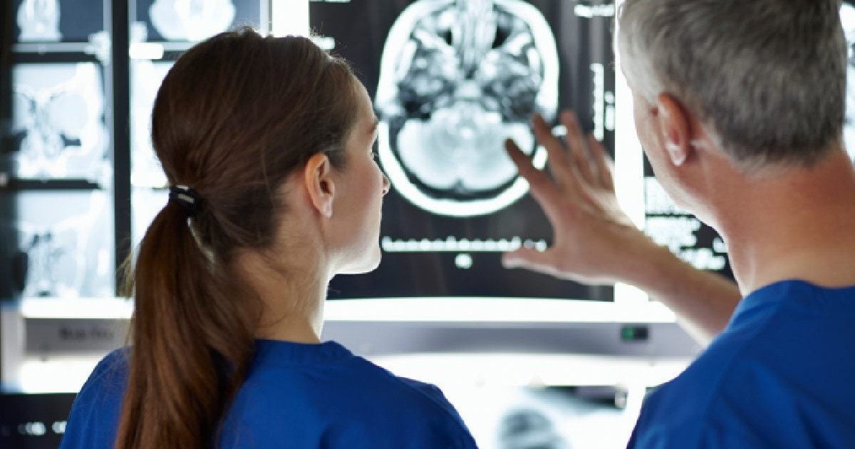 doi medici o femeie si un barbat imbracati in uniforme de spital se uita la o imagine cu un creier, neurochirurgii „harta creierului” înainte de operație
