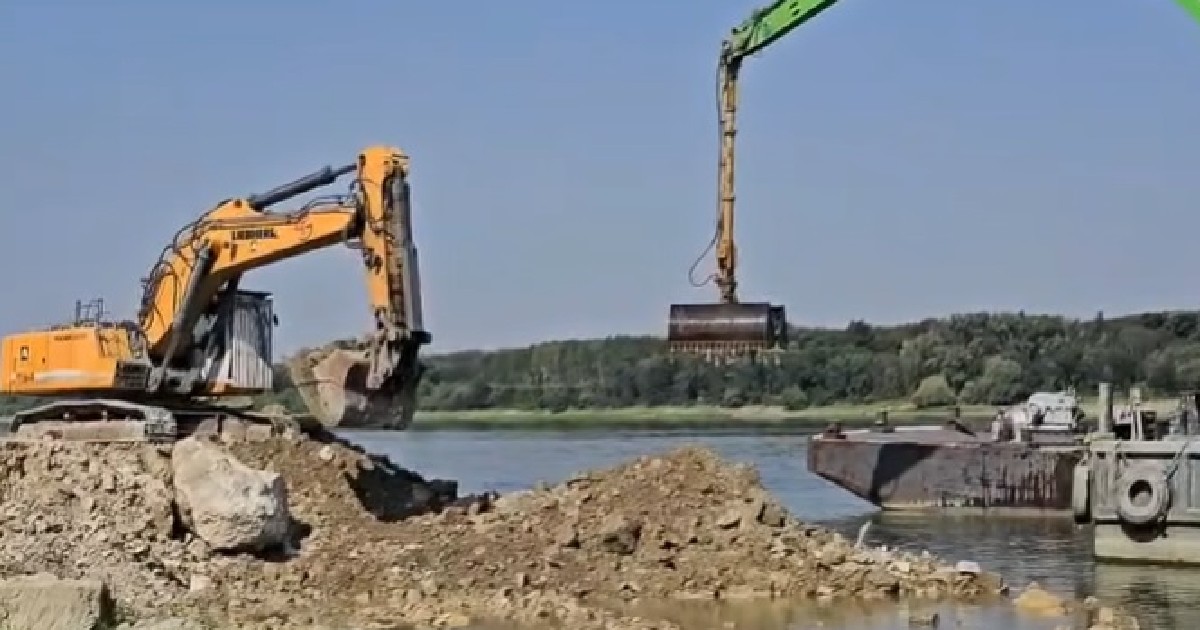 Excavatoare care umplă o barjă cu piatră și stâncă
