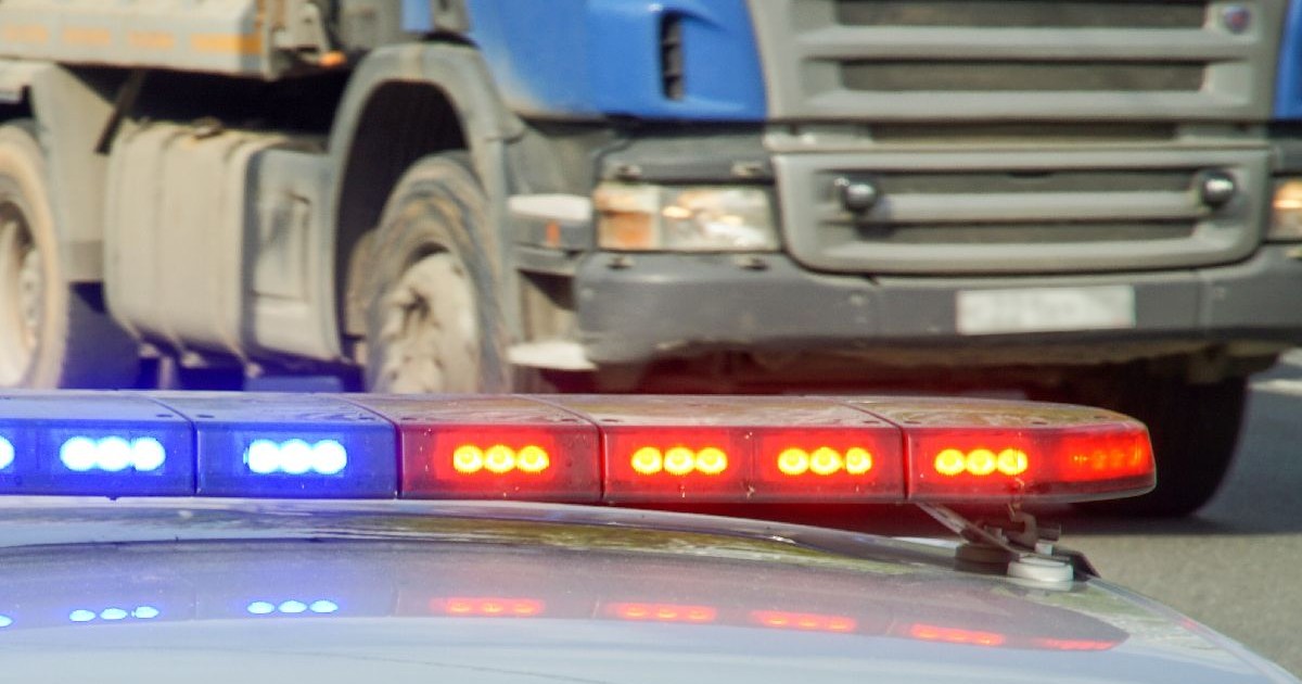Fotografie cu luminile albastre și roșii intermitente ale unei mașini de poliție pe o autostradă, cu un camion albastru mare în fundal.