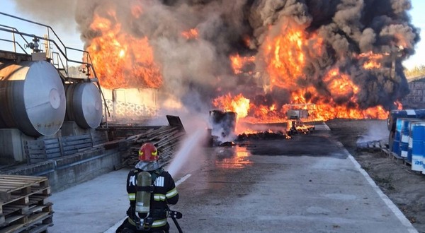 În curtea unei hale industriale, un pompier echipant cu aparat de respirat stă în genunchi pe o platformă betonată și direcționează un jet de apă spre un incendiu violent, sutești, valcea, 3 octombrie 2026