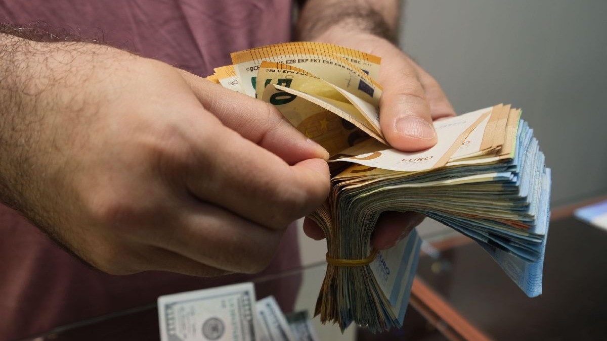 Un bărbat îmbrăcat cu un tricou mov ține în mâini bancnote euro