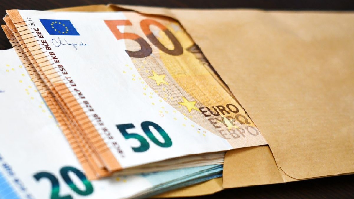Bancnote de 50 și 20 de euro într-un plic maro pe masă.